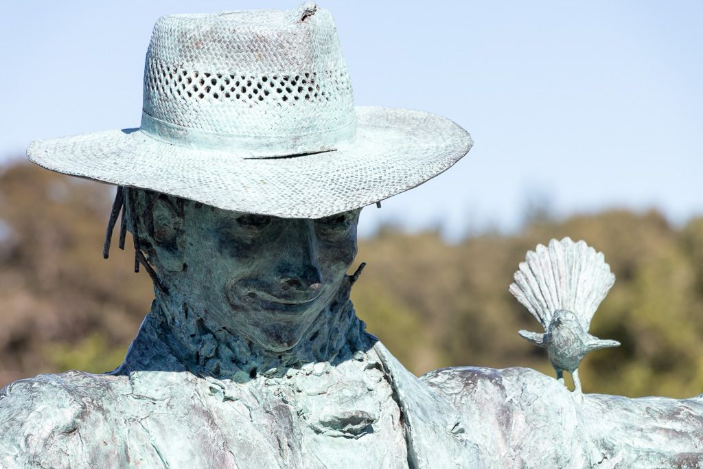 A Bronze scarecrow at the Kitchen Garden with a Fan-Tail hanging out on his shoulder.